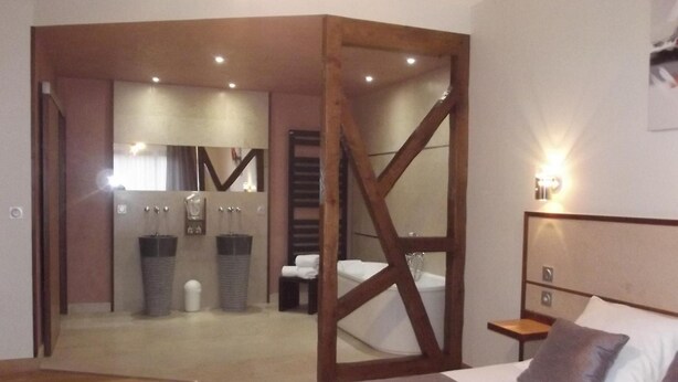Een hotelkamer met een houten vloer, een bed met een grijze deken, een nachtkastje en een wandlamp.