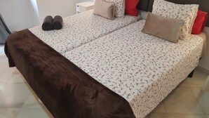 A double bed with floral bedding, two nightstands, a brown throw blanket, and a pair of shoes on the floor. - Fan Rooms Duquesa (Málaga)