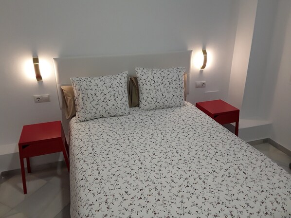 A bedroom with a floral bedspread, two red nightstands, and wall-mounted lights.