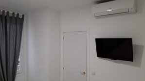 A room with a white door, a mounted flat-screen TV, and an air conditioning unit on the wall. - Fan Rooms Duquesa (Málaga)