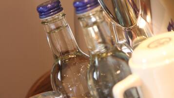 Primer plano de varias botellas de vidrio con tapones azules, probablemente conteniendo bebidas, y un recipiente blanco con un logo, posiblemente para servir o guardar.