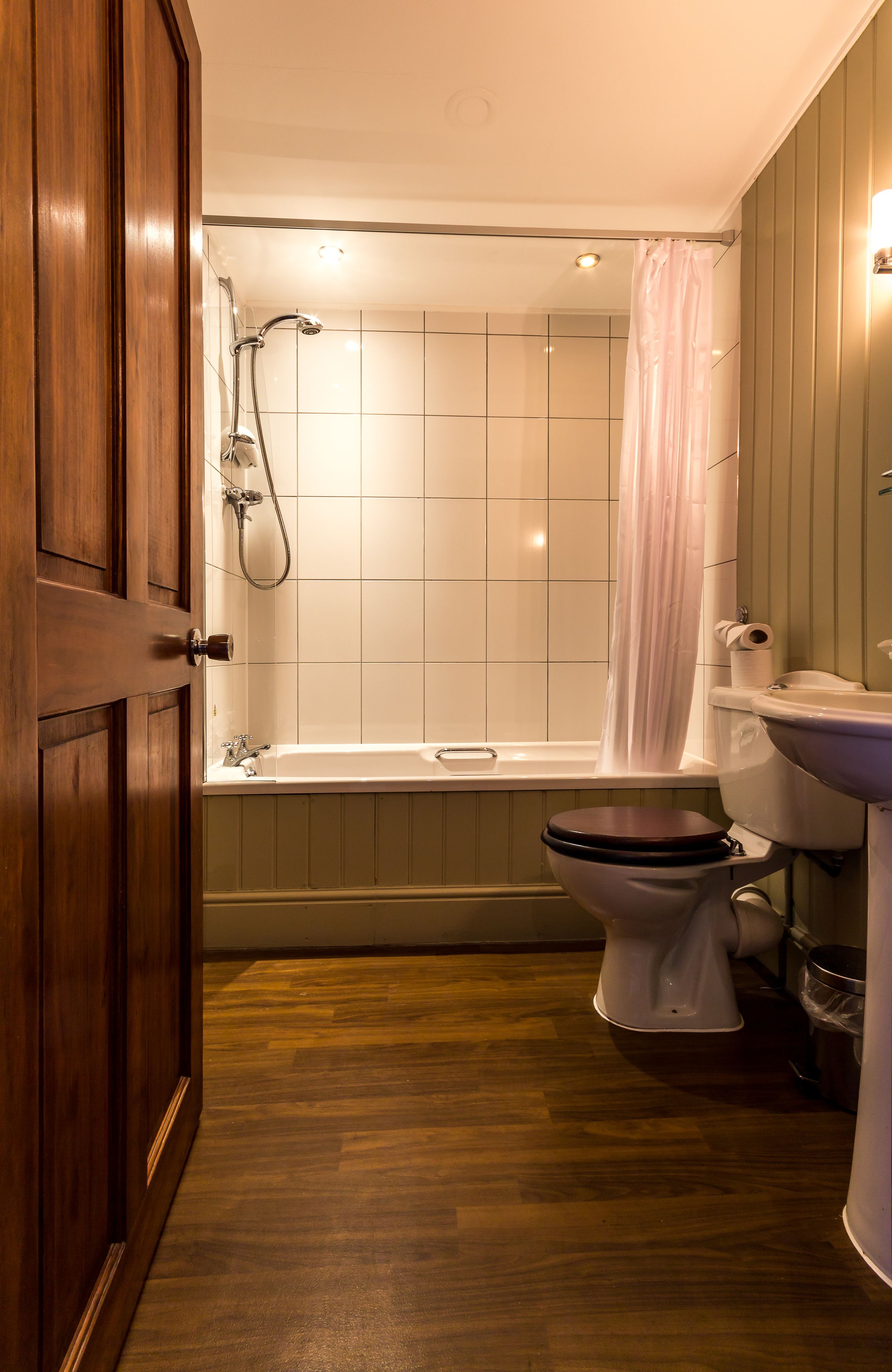 A bathroom with a wooden door, a bathtub, a toilet, and a sink.