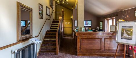 Un vestíbulo de hotel con una imponente escalera, una recepción y una fotografía enmarcada.
