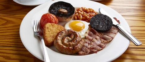 A breakfast plate with eggs, bacon, sausages, tomatoes, beans, and toast on a wooden table.