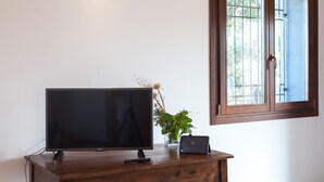 A television on a wooden stand, a remote control, and a small potted plant on a white wall. - Etnella enoagriturismo Notti Stellate (Mascali)