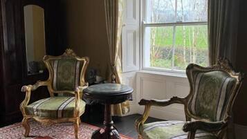 A room with two ornate chairs, a small round table, and a large window with curtains.