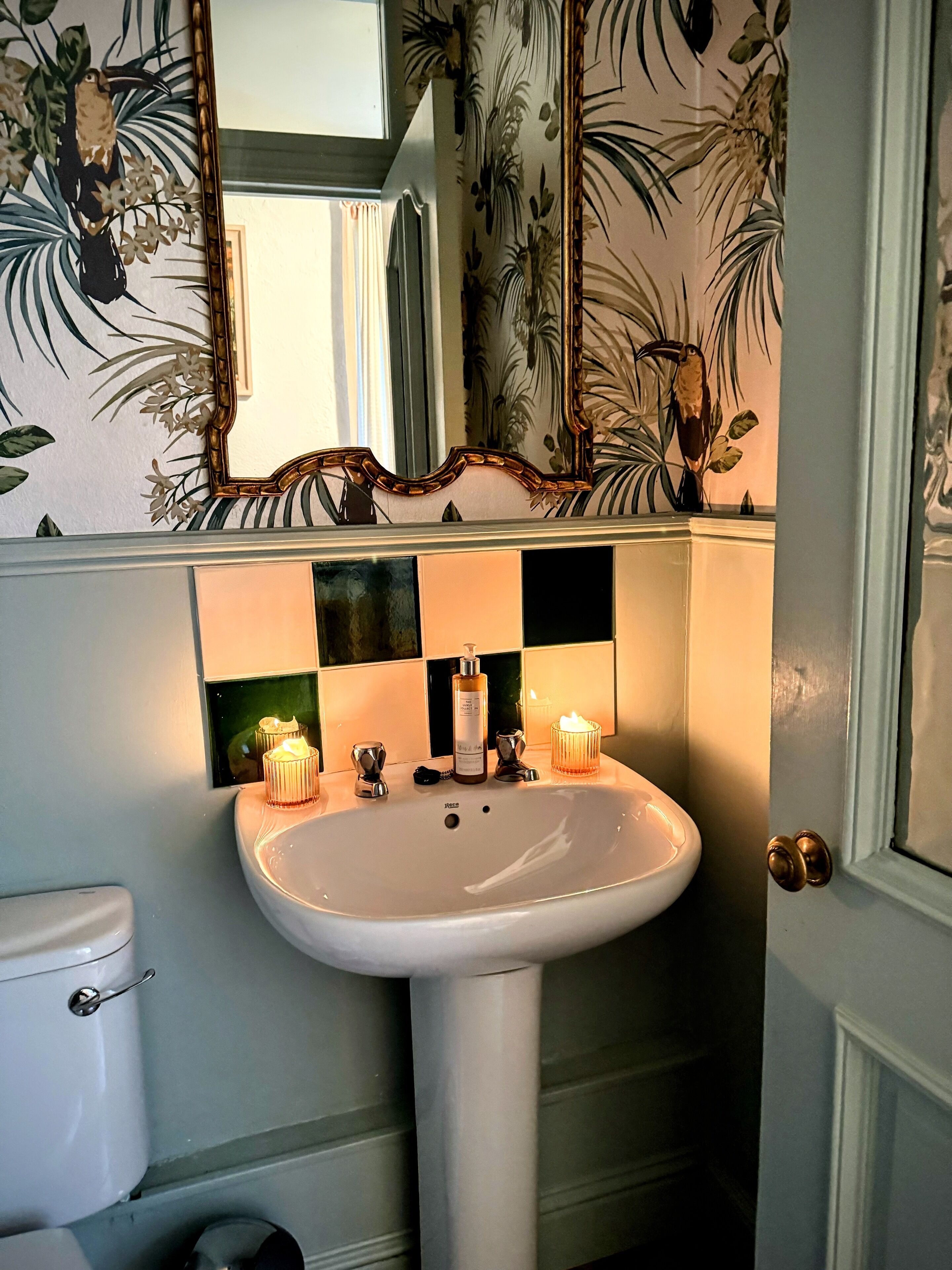 Un baño con un lavabo pedestal blanco, dos velas encendidas y un espejo encima.