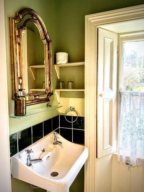 A bathroom with a white sink, a mirror, and shelves with toiletries. - Clone House (Aughrim)