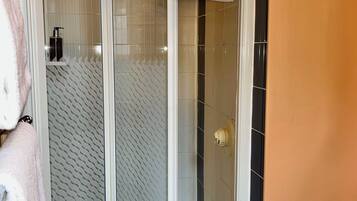 A shower with a glass door, a towel hanging on the door, and a toilet visible to the right.
