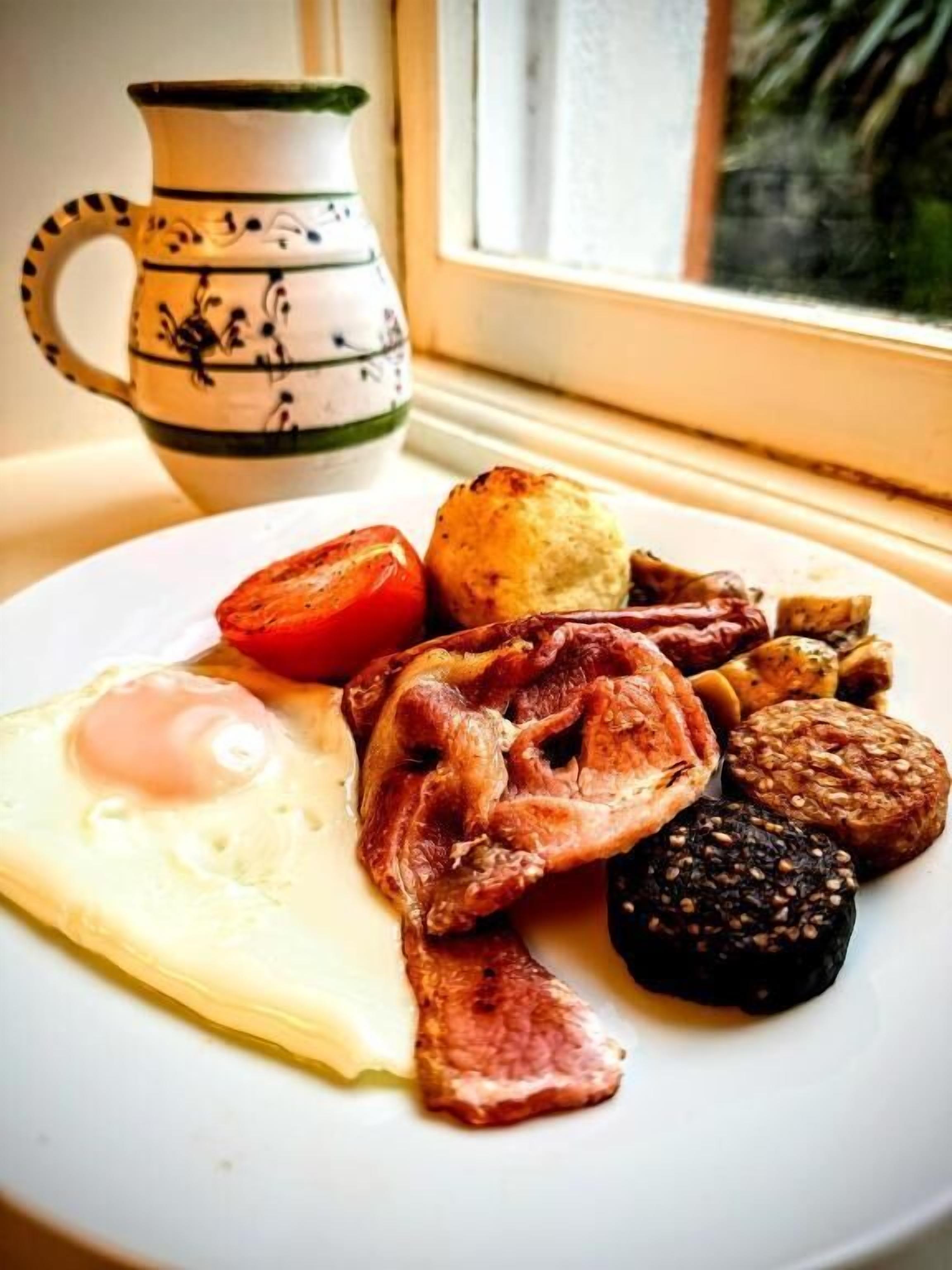Un plato de desayuno con huevos, tocino, salchichas y tomate.