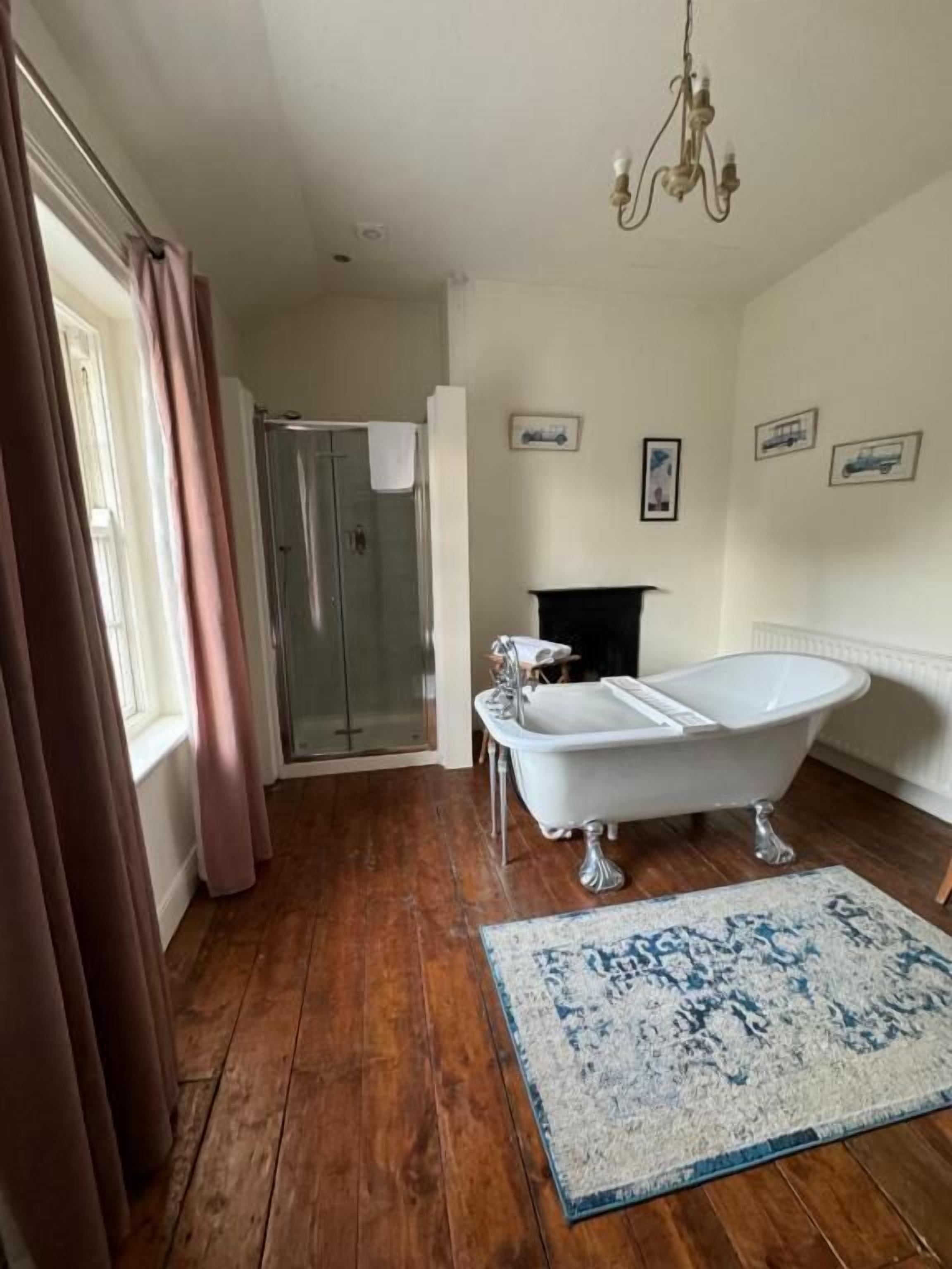 Un baño con bañera tipo pata de león, suelo de madera, cabina de ducha de vidrio y un candelabro.