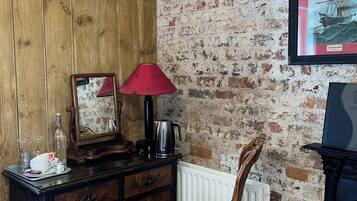 A room with a wooden dresser, a red lamp, a chair, a mirror, and a framed picture of a ship on the wall.