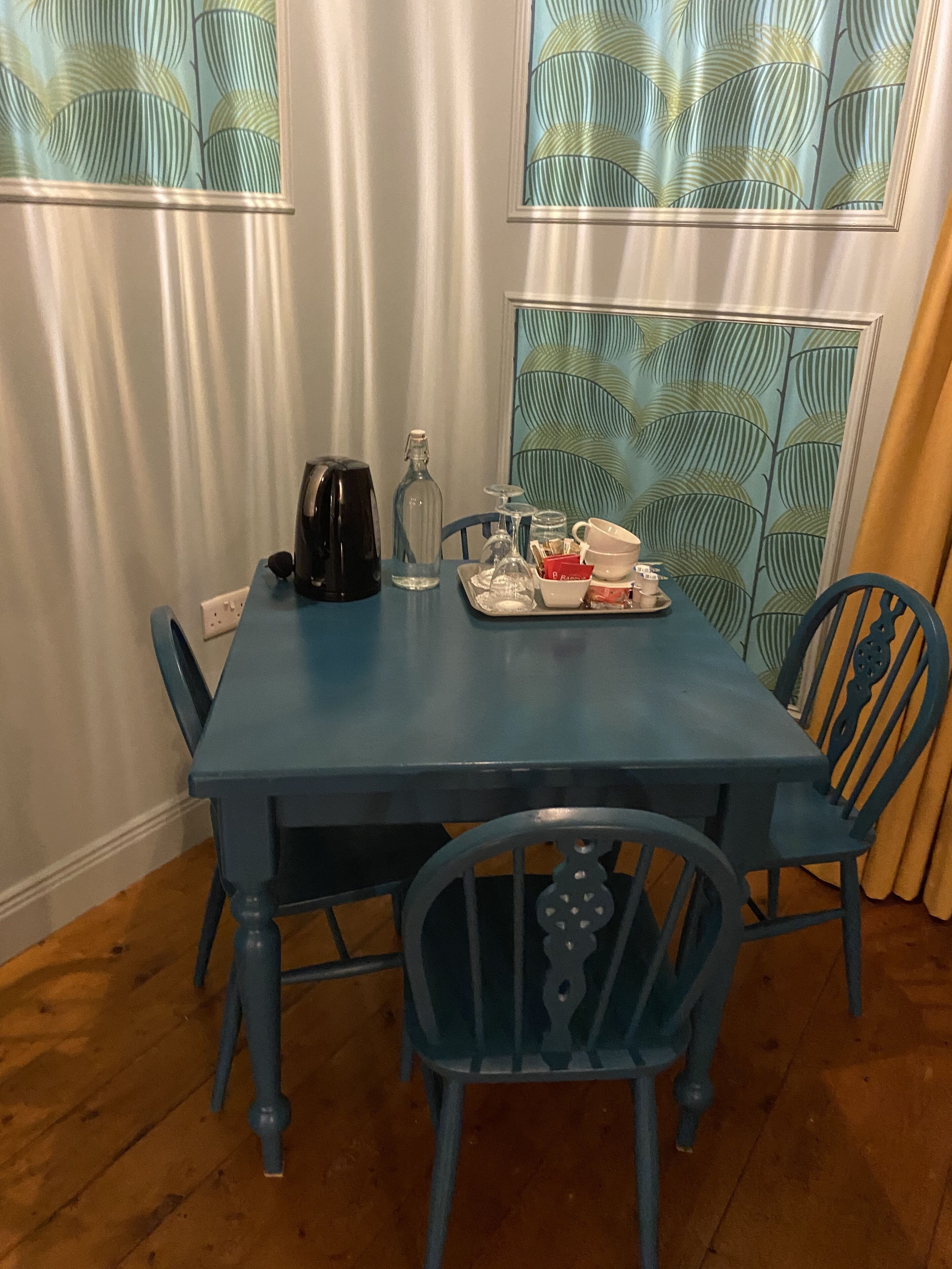 Una mesa de comedor con sillas, una tetera, una botella y una bandeja con platos.