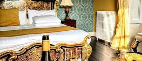 A bedroom with a large bed, a nightstand, a bottle of champagne, and two glasses on a marble table.
