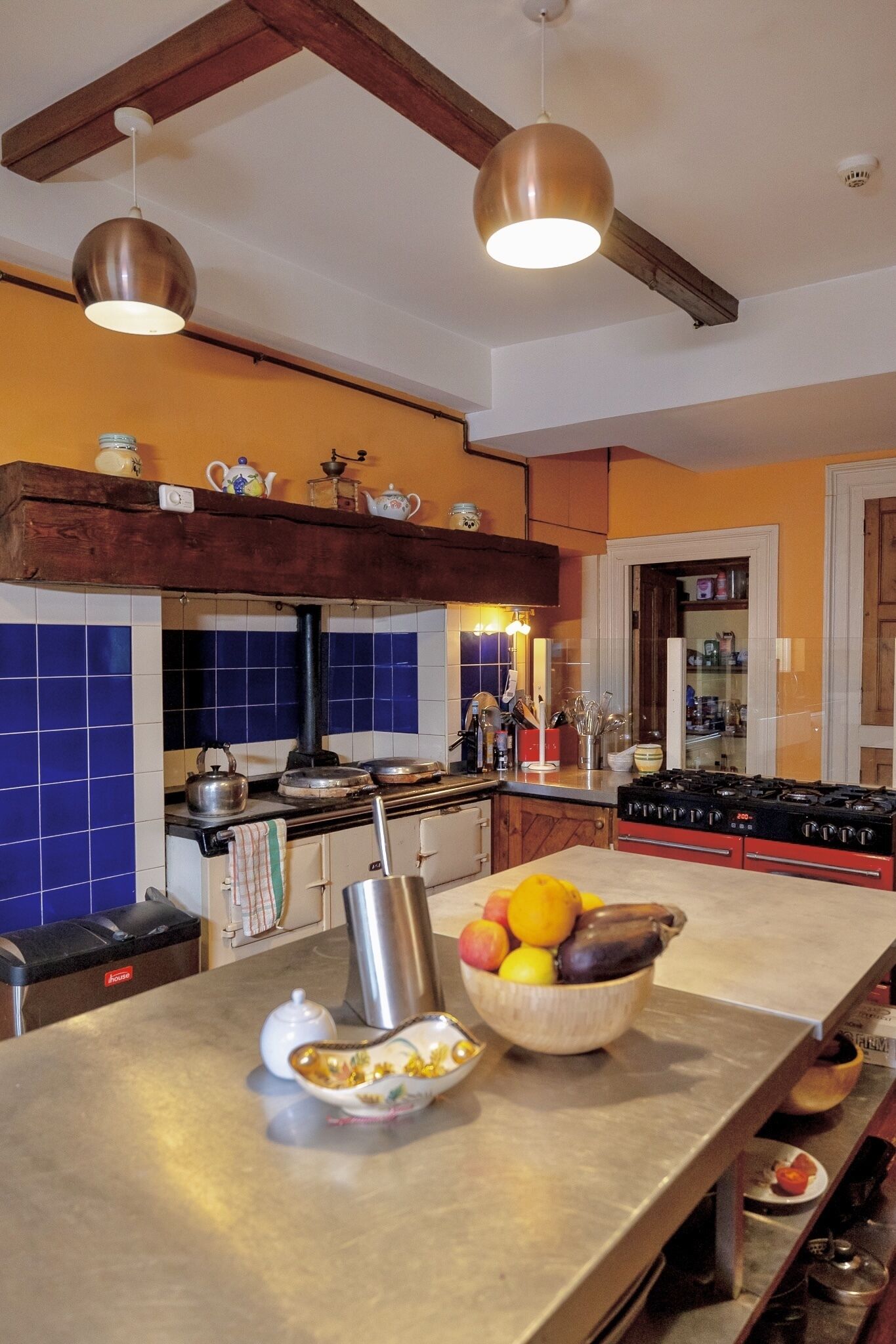A kitchen with blue tiles, a stove, and a fruit bowl on the counter.