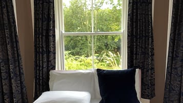 Un dormitorio con cama, ropa de cama blanca, colcha acolchada azul oscuro y una ventana con cortinas.