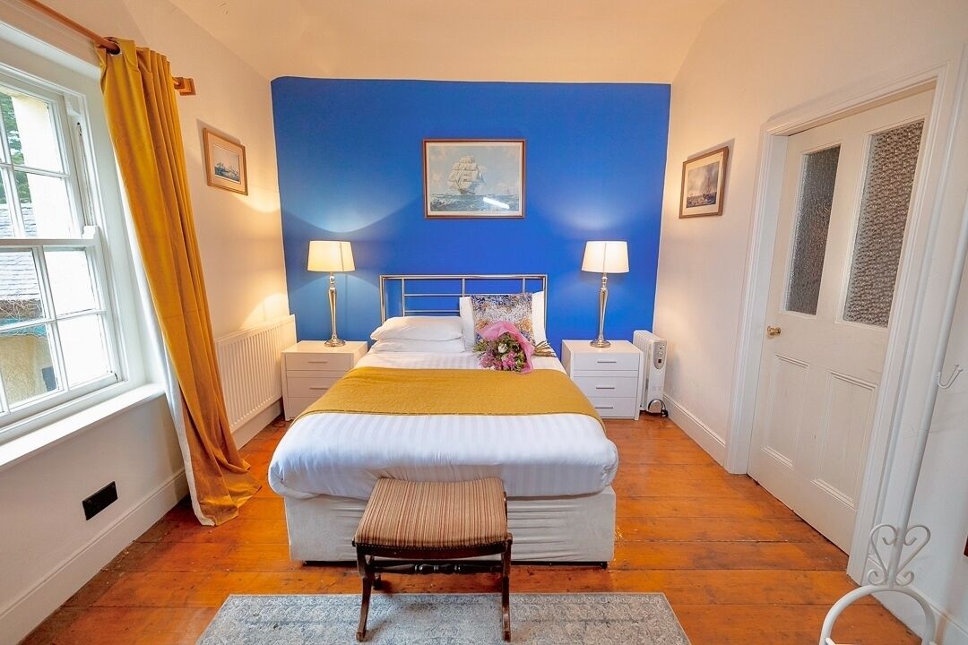 Un dormitorio con cama, mesitas de noche, una ventana con cortinas y una pared azul.