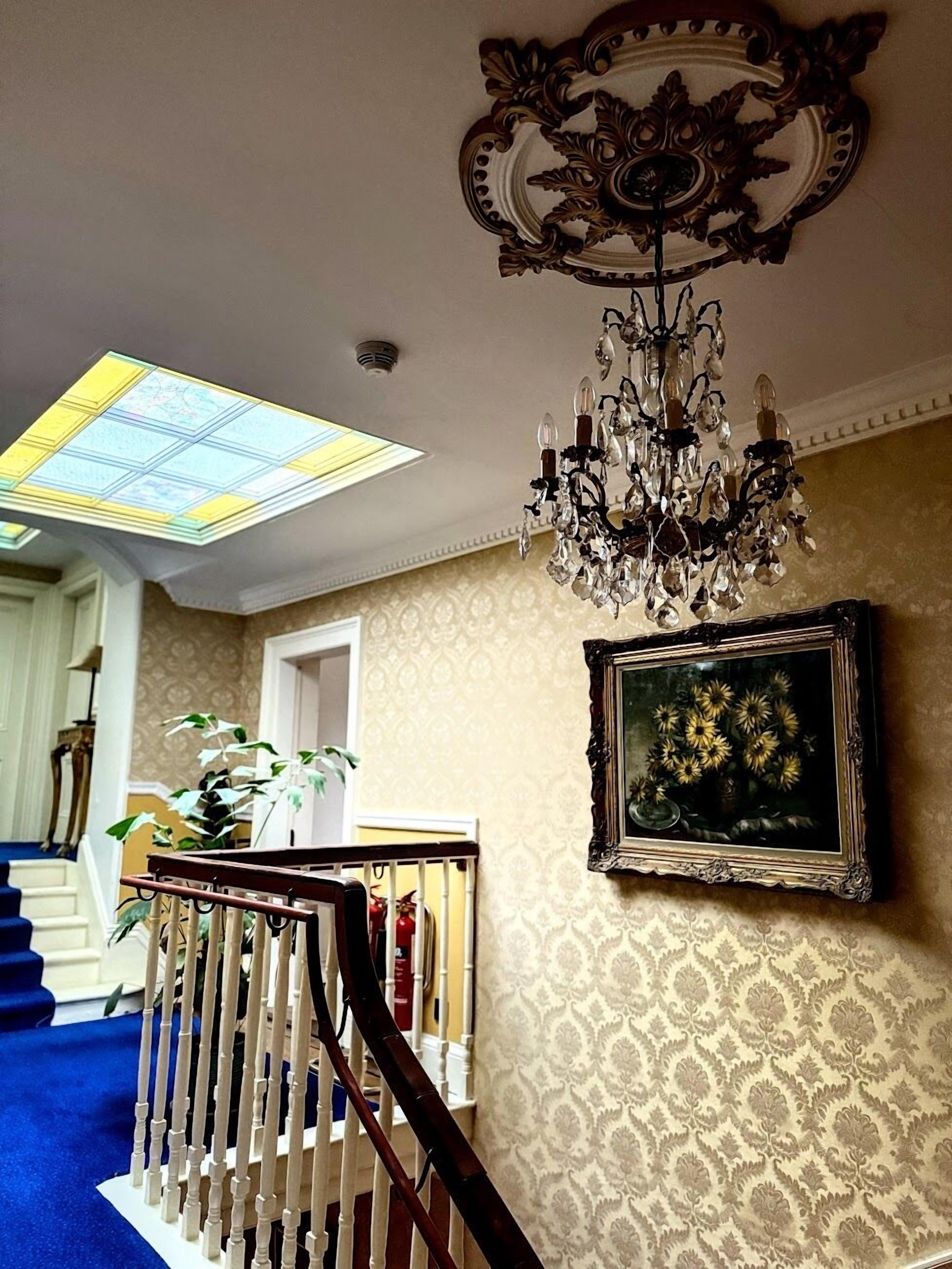 Una escalera con barandilla de madera, un candelabro, un cuadro enmarcado y un papel tapiz estampado.