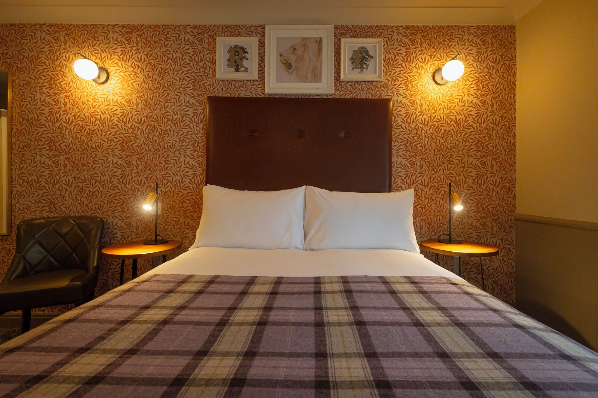 A hotel room with a large bed, two bedside tables, a chair, and patterned wallpaper.