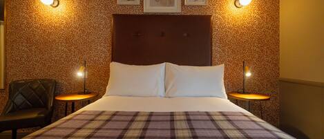 A hotel room with a large bed, two bedside tables, a chair, and patterned wallpaper.
