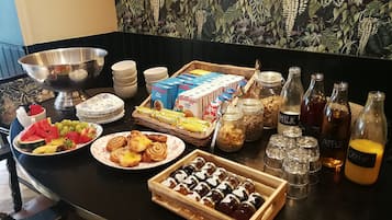 A buffet table with various food items, including fruits, pastries, cereals, and beverages.