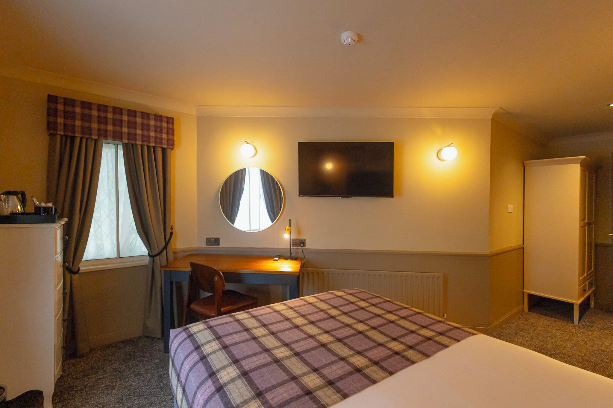 A hotel room with a bed, desk, chair, television, and a radiator.