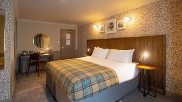 Une chambre d’hôtel avec un lit, un bureau, une chaise, un miroir rond et un mur recouvert d’un papier peint à motifs.