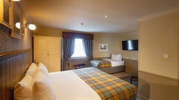 A hotel room with a large bed, a smaller bed, a TV, and a window with curtains.