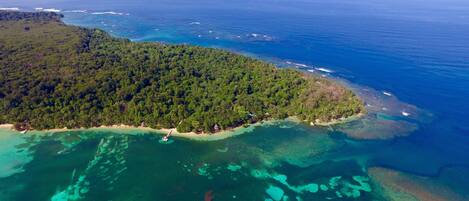 An aerial view of a tropical island with dense forest, clear blue waters, and visible boats.