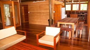 Una habitación amplia con piso de madera, una mesa de comedor con bancos, un sofá y una zona de cocina con armarios de madera y un lavamanos.