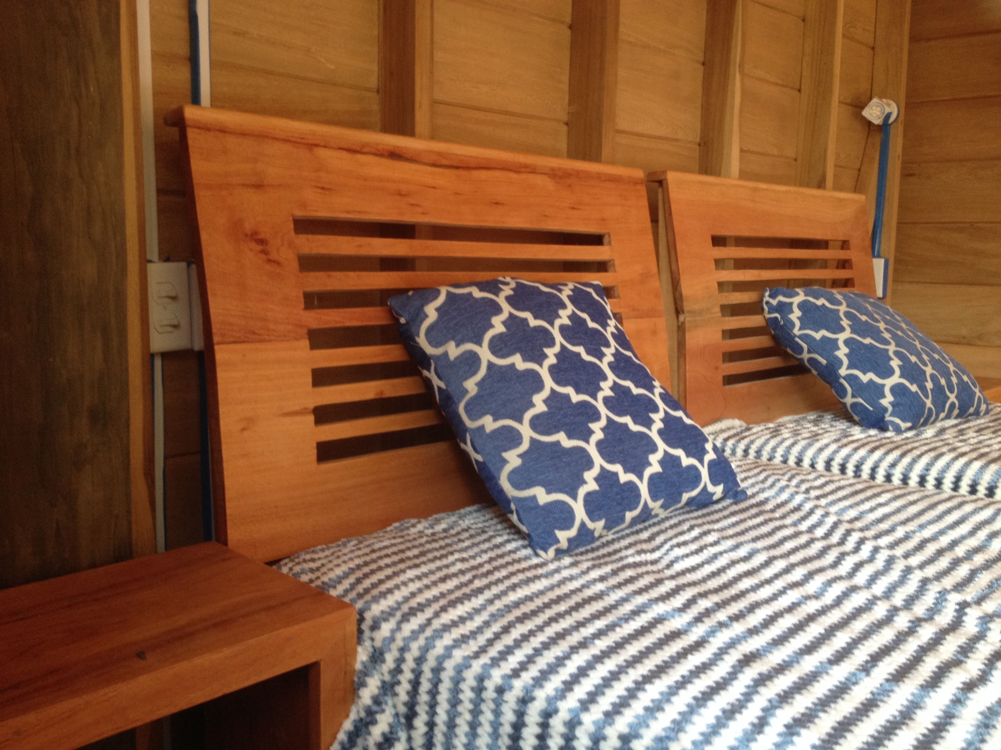Una cama de madera con cabecera, dos almohadas estampadas y una colcha a rayas.