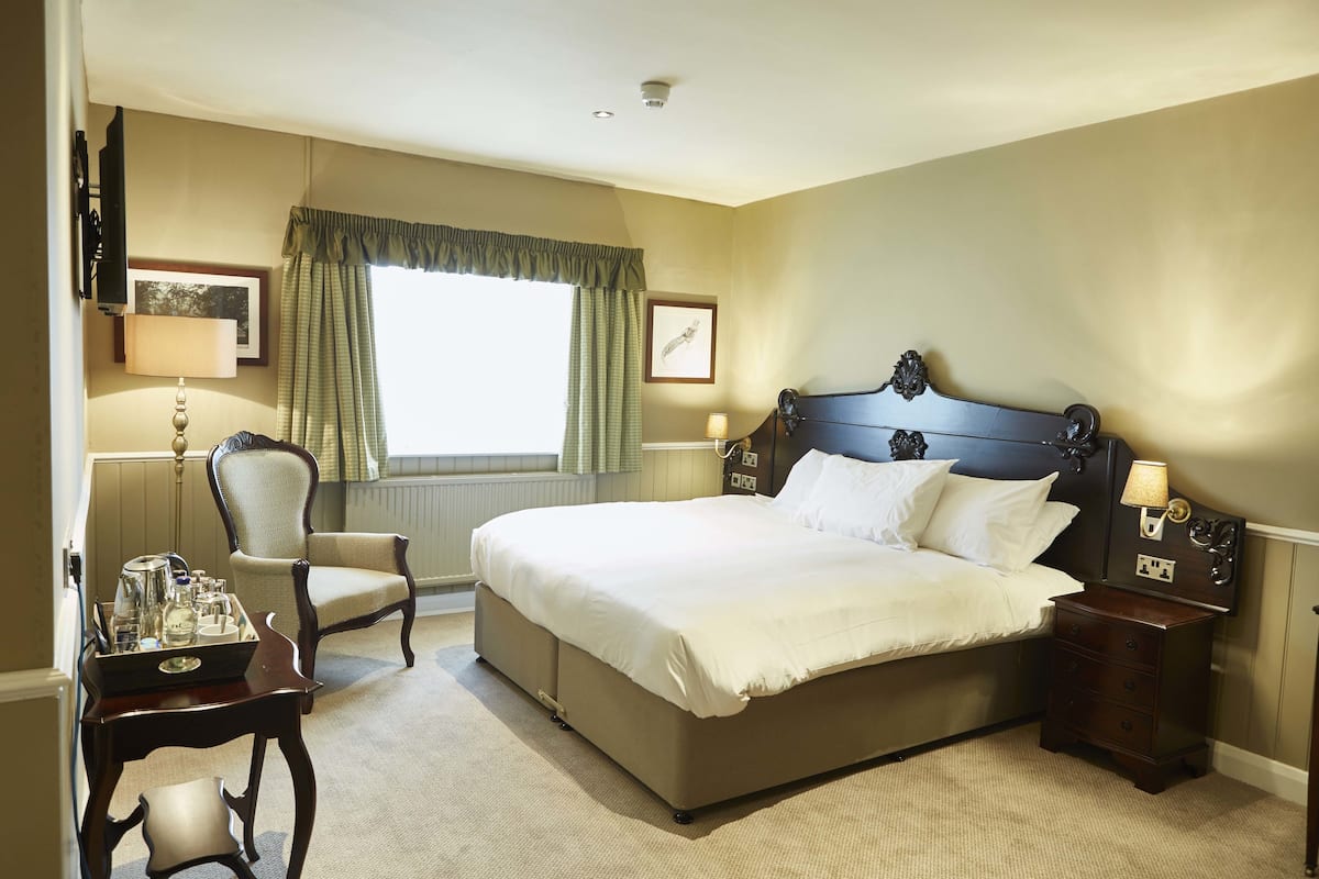 A neatly arranged hotel room with a large bed, a chair, a bedside table, and a window with curtains.
