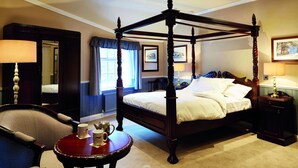 A four-poster bed with a wooden frame, a round table with a red top, and a chair with a high backrest. - The Golden Pheasant (Knutsford)