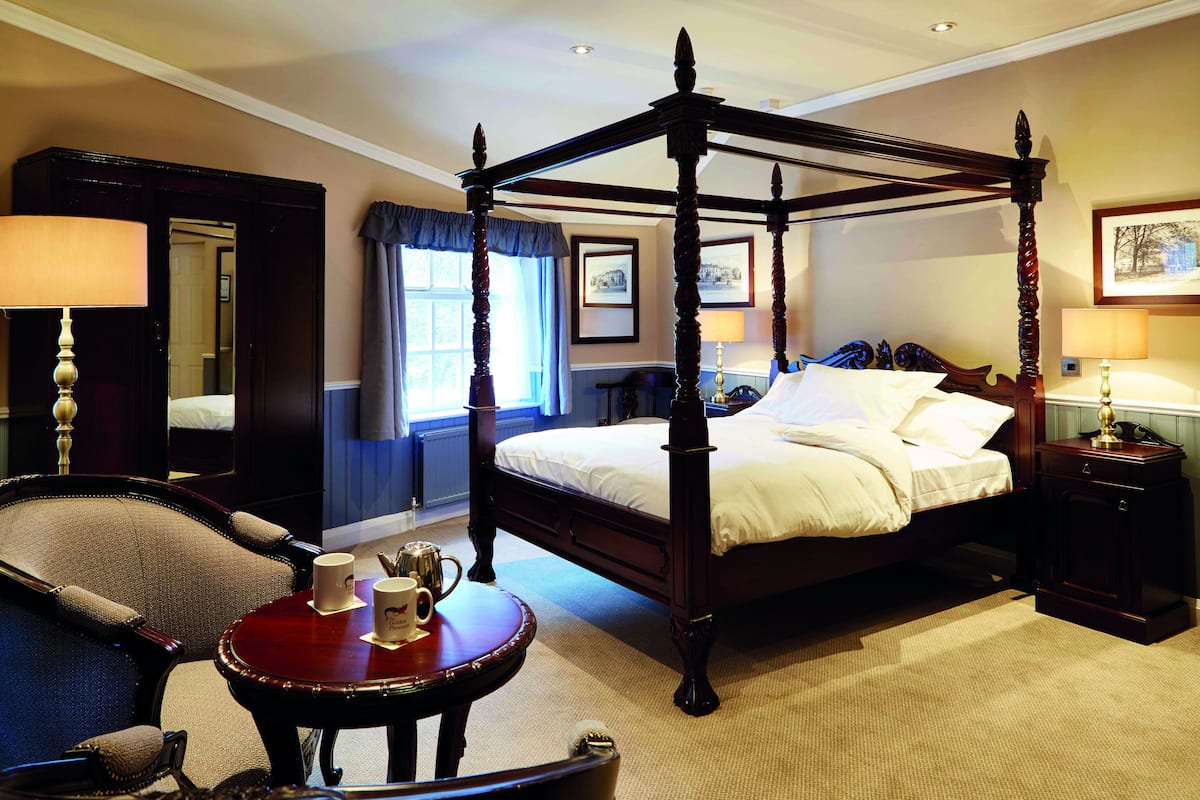 A four-poster bed with a wooden frame, a round table with a red top, and a chair with a high backrest.