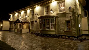 A traditional building with multiple windows, a stone-paved entrance, and a small covered area with a bench. - The Golden Pheasant (Knutsford)