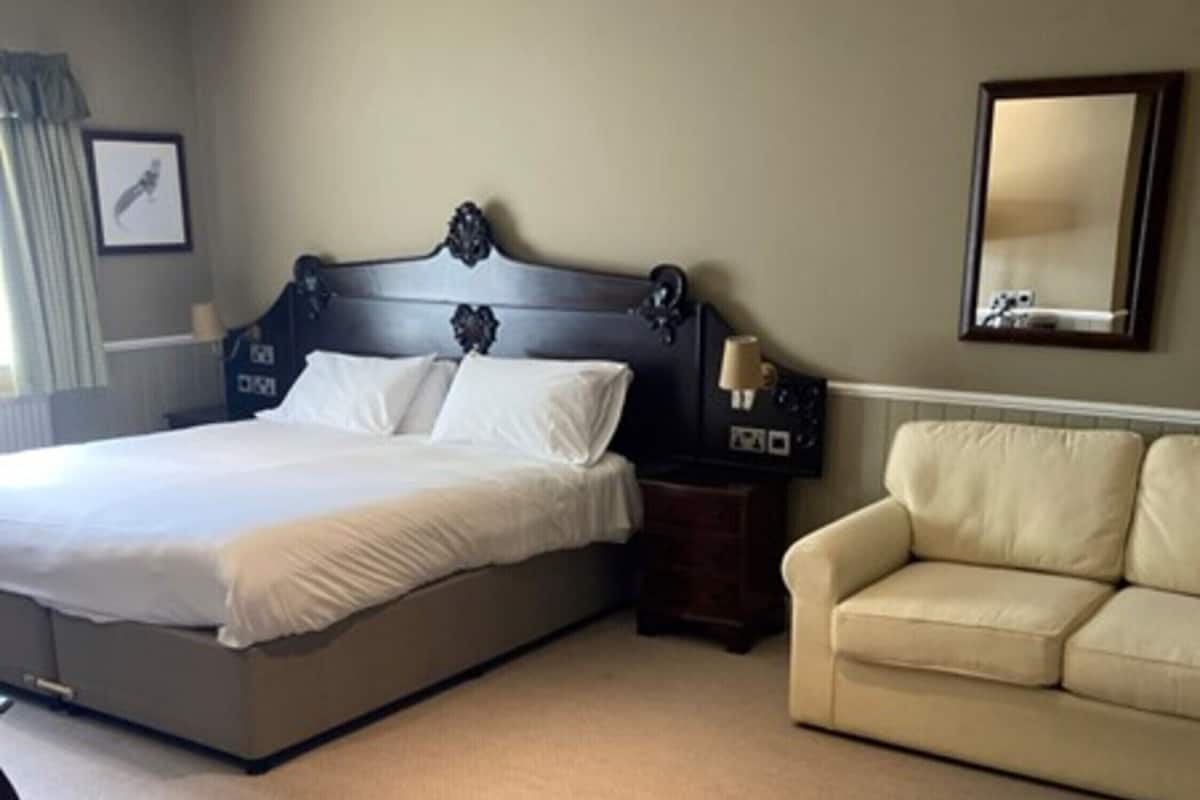 A hotel room with a large bed, a bedside table, a lamp, a sofa, and a framed picture on the wall.