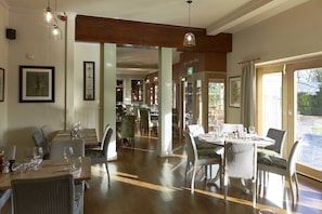 A restaurant with wooden tables and chairs, framed artwork on the walls, and large windows allowing natural light. - The Golden Pheasant (Knutsford)