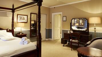 A four-poster bed with rolled towels, a desk with a mirror, a chair, and a lamp.