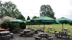 An outdoor patio area with multiple wooden picnic tables and green umbrellas, some with 'Carlsberg' branding. - The Golden Pheasant (Knutsford)