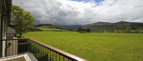 Un balcón con vista a un campo verde y colinas.