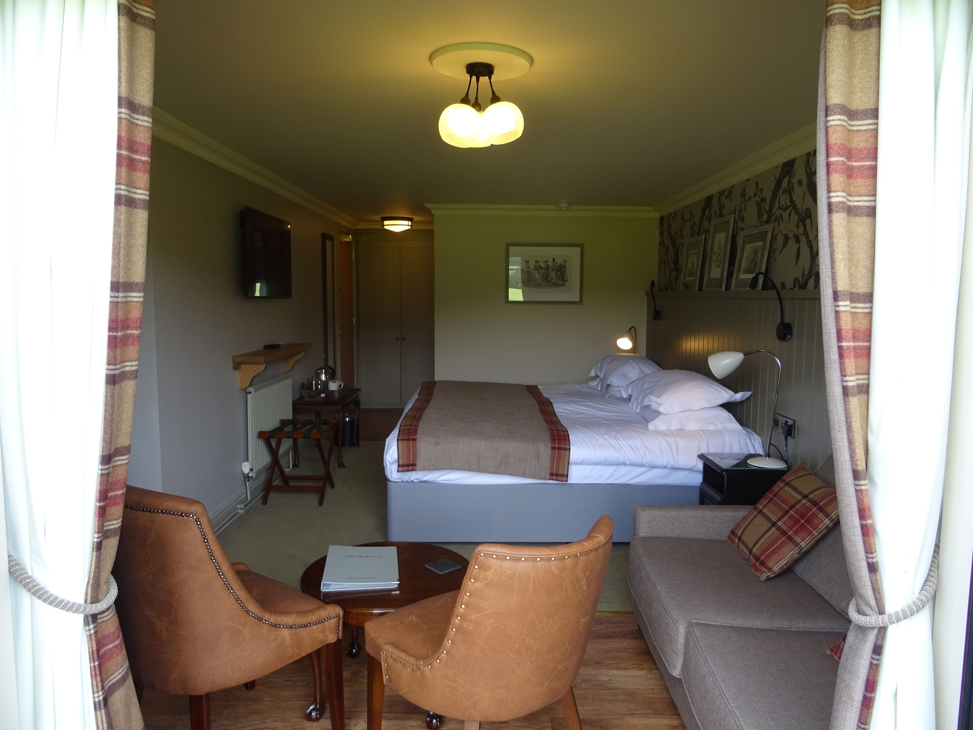 A hotel room with a bed, a desk, a chair, a sofa, and a ceiling light.
