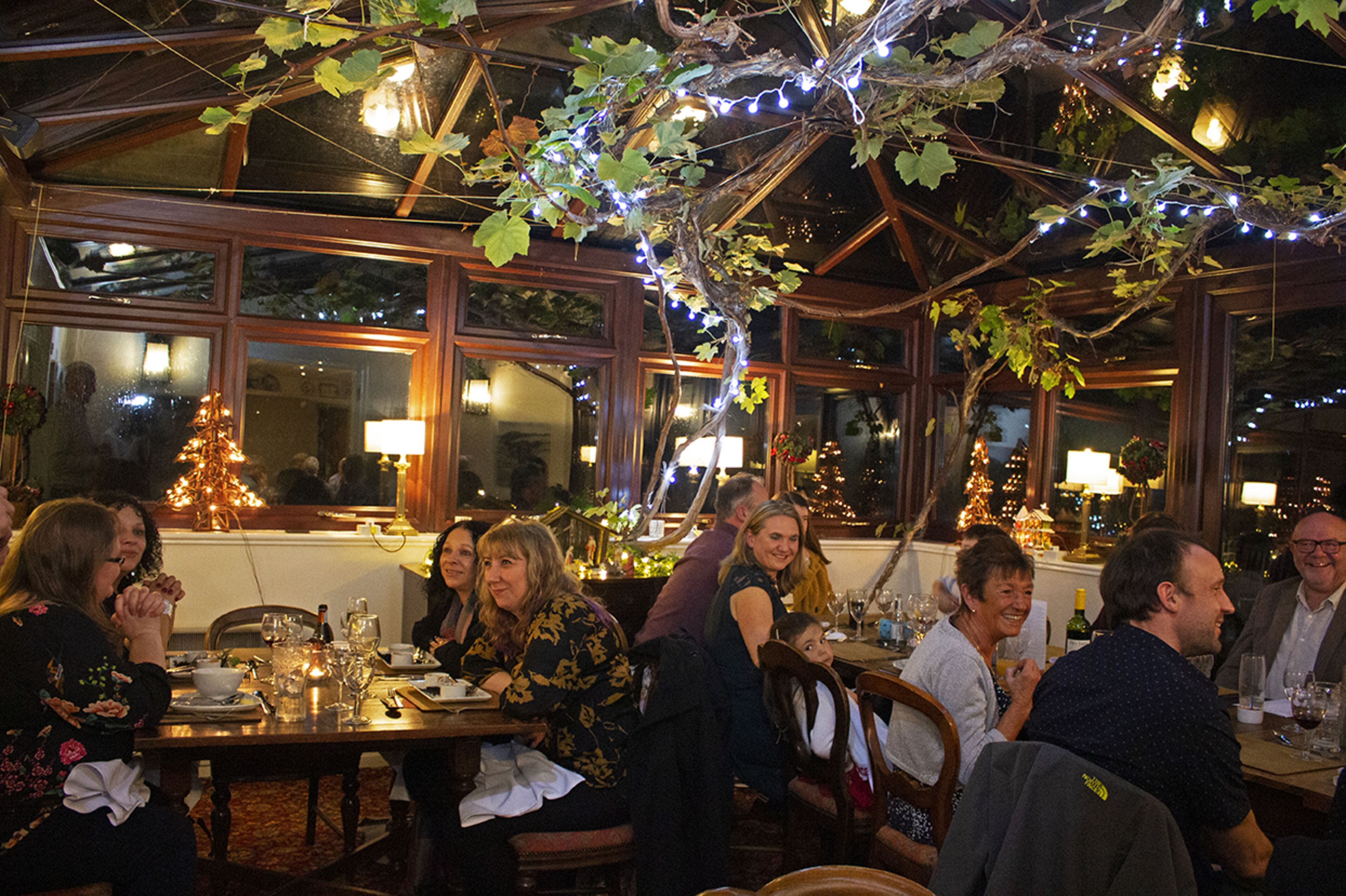 Een restaurant met glazen plafond, houten tafels en lichtslingers.