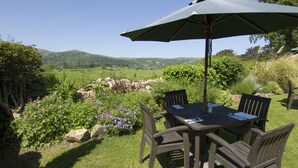 An outdoor dining area with a table and chairs, an umbrella, and a view of a green landscape with hills. - The Groes Inn (Conwy)