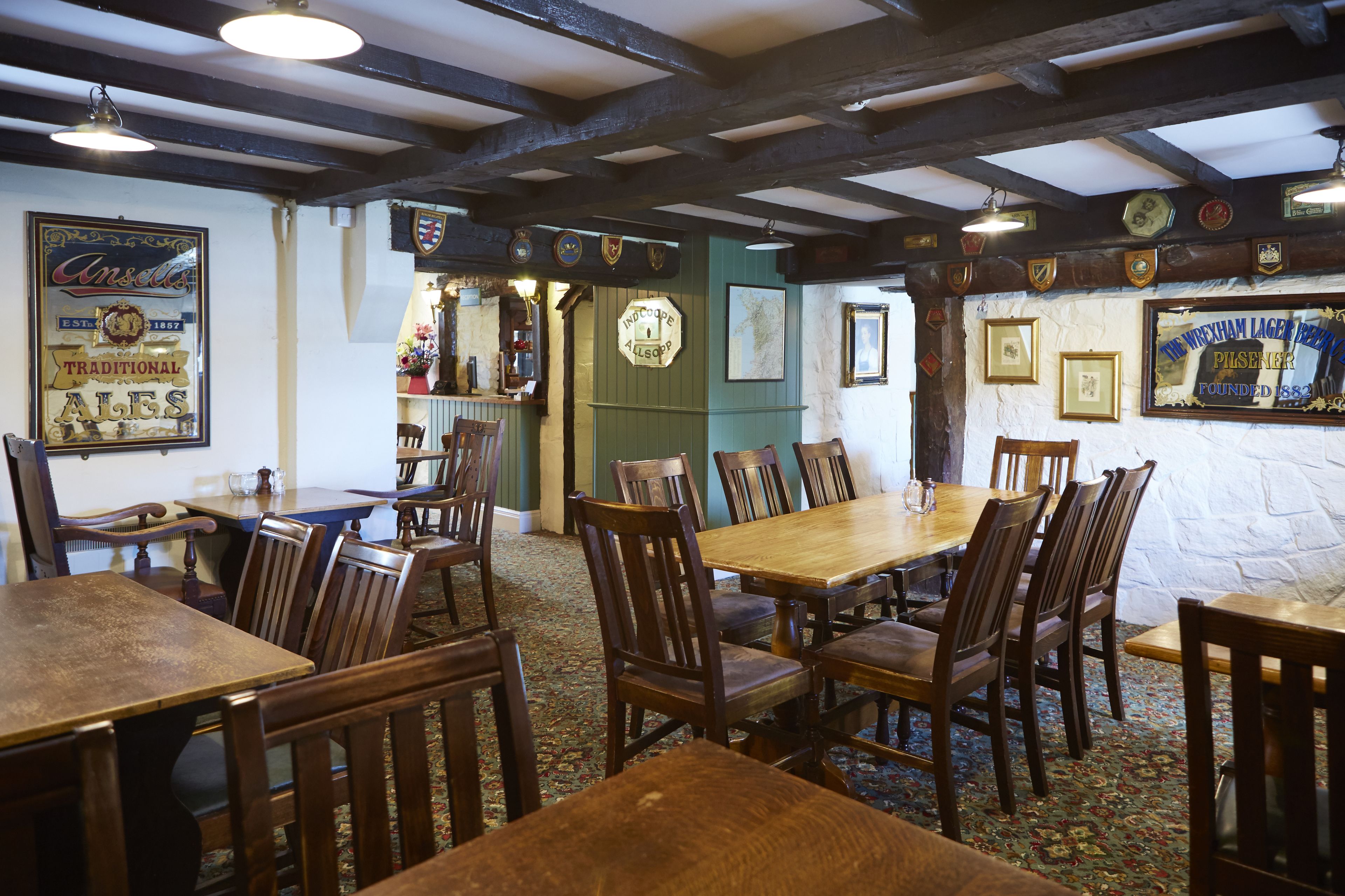 A traditional pub interior with wooden tables and chairs, a bar area, and various framed pictures and signs on the walls.