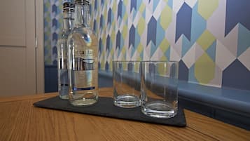 Dos botellas y dos vasos sobre un posavasos de pizarra en una mesa de madera.