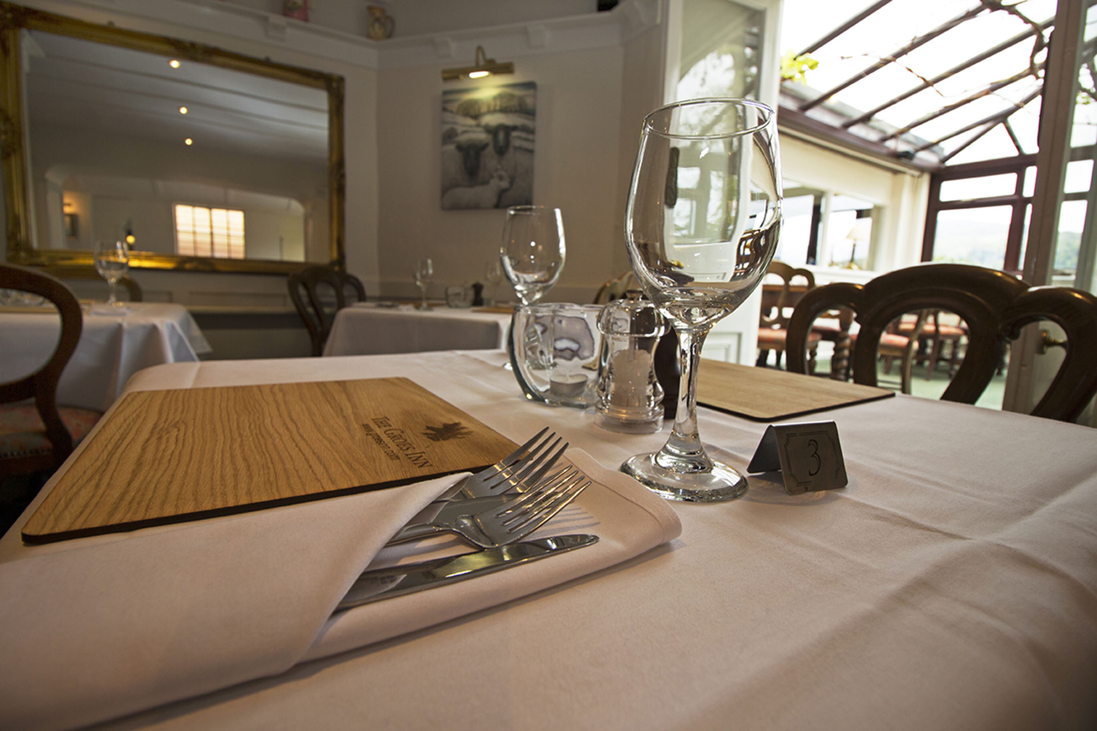 A dining table set with a menu, cutlery, and wine glasses, with a number card on the table.