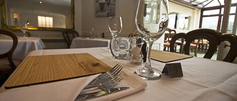 Uma mesa de jantar posta com menu, talheres e copos de vinho, com um cartão de número sobre a mesa.