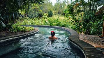 A person in a hot tub surrounded by lush greenery.