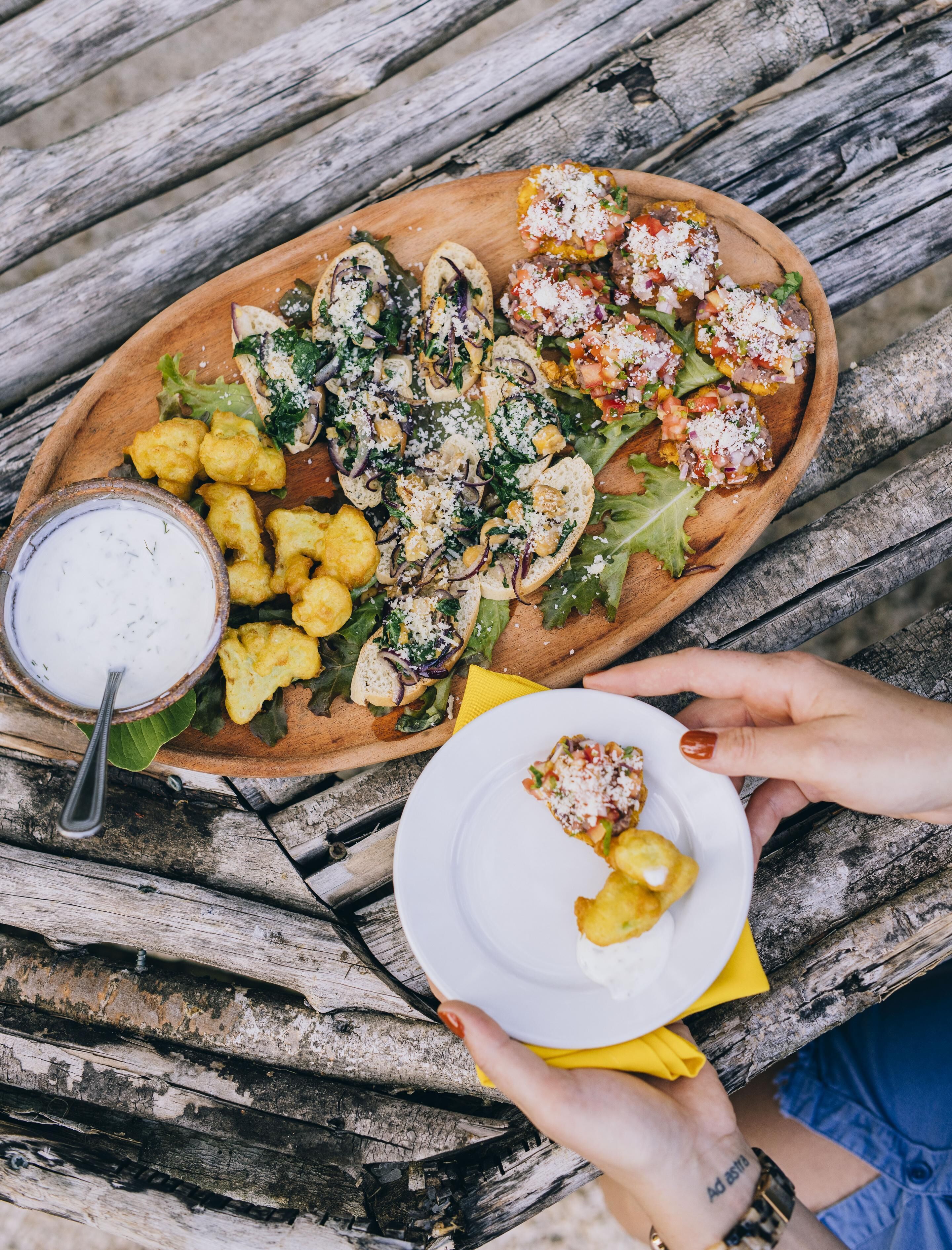 A wooden table with a variety of food items, including bread, salad, and a bowl of dip.