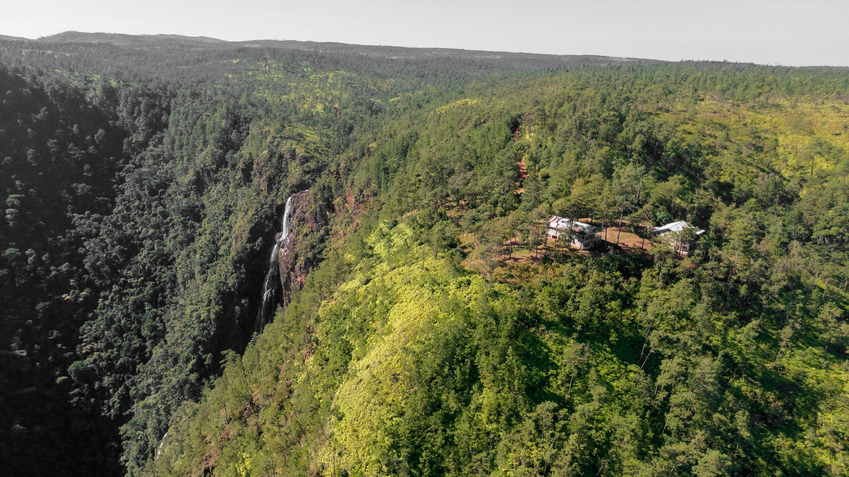 An aerial view of a forested area with a waterfall and a small cluster of buildings.